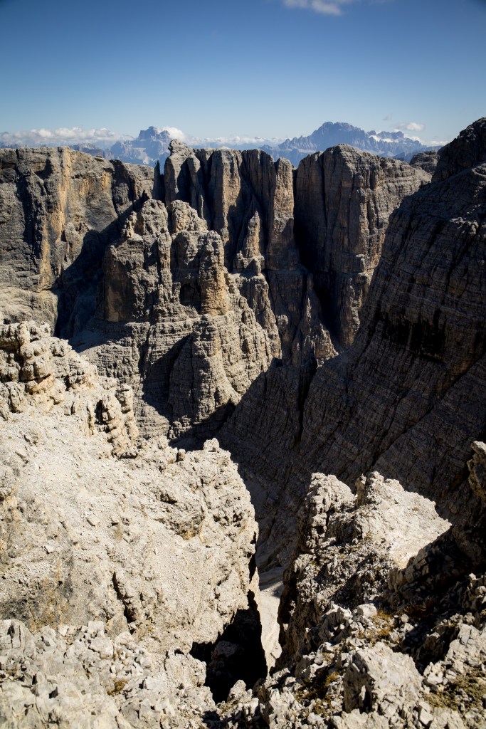 A scenic view of rugged mountainous terrain with steep rock formations and a deep valley under a clear blue sky.