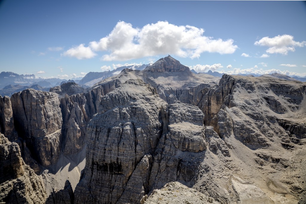 A panoramic view of rugged mountains with sharp peaks under a clear blue sky, featuring rocky terrain and distant mountain ranges.